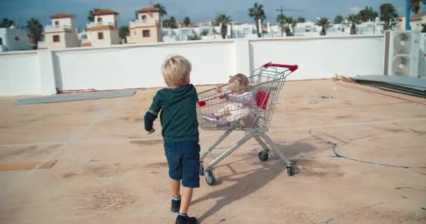 Los niños se divierten jugando con el carrito de remojo de supermercados en el estacionamiento al aire libre — Vídeo de stock