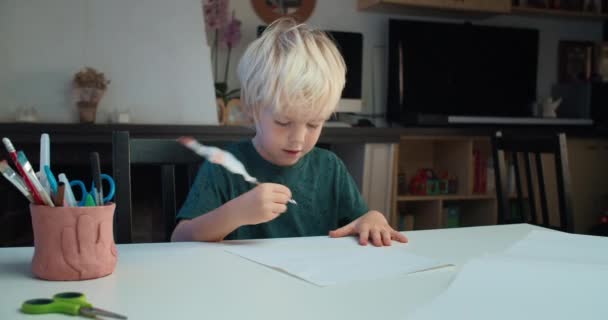 Niño lindo sentado en la mesa y dibujando con pluma de pluma en la sala de estar — Vídeos de Stock