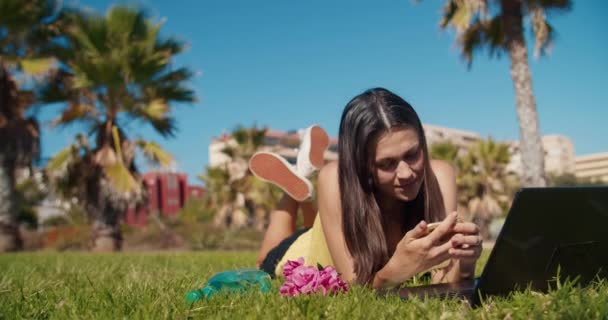 Gelukkig aantrekkelijke freelance vrouw liggend op openbaar park met behulp van smartphone — Stockvideo