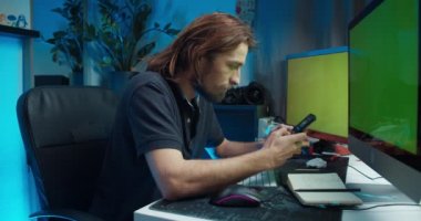 Young freelance worker sitting in front of computer typing message in smartphone