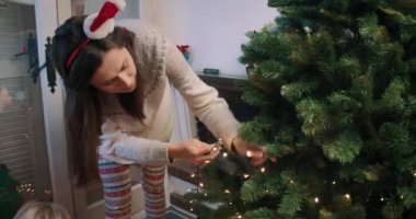Genç ve çekici bir kadın Noel ağacını süslüyor çelenk ışıkları takıyor