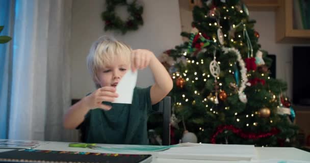 Lindo niño cortando papel regalo de Navidad hecho a mano usando tijeras — Vídeos de Stock