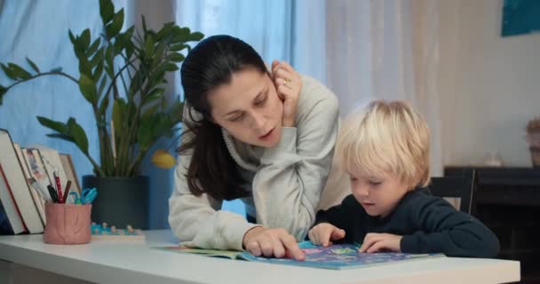 Молода мати з дошкільним хлопчиком читає книгу з лабіринтами — стокове відео