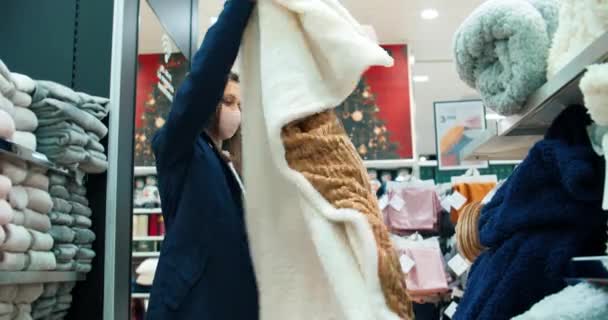 Young woman wearing medical face protection mask on shopping choosing bedspread — 图库视频影像