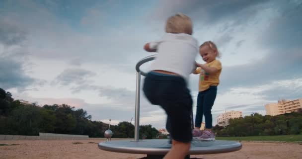 Bratr a sestra se baví na kolotoči v parku — Stock video