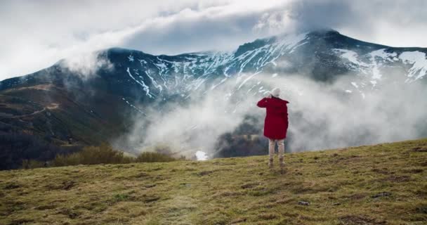Young adult woman standing on top of the mountain expecting floating clouds — Vídeo de stock