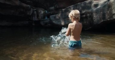 Çocuk dağdaki nehirde şelaleyle oynuyor.