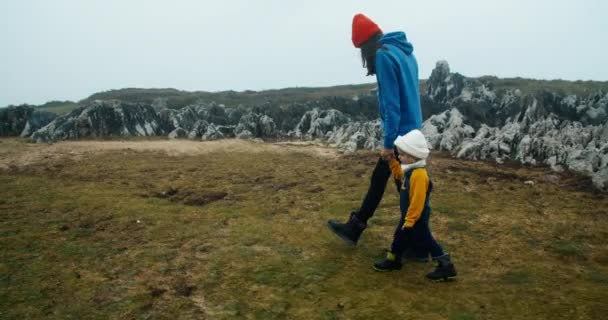 Молода доросла жінка гуляє з дочкою на березі океану за скелею — стокове відео