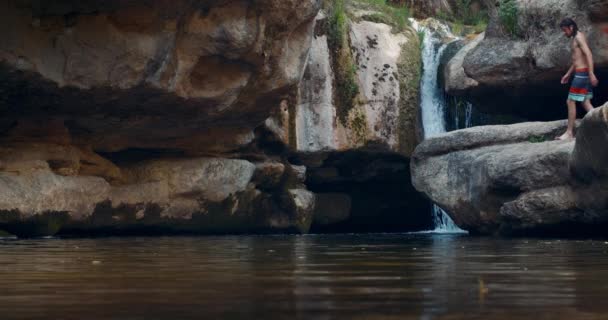 Туристичний чоловік стрибає і занурюється в річку зі скелі — стокове відео