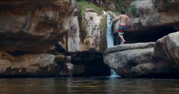 Mann steht vor Wasserfall und hebt die Hände — Stockvideo