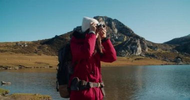 Göl kıyısında seyahat eden kadın fotoğrafçı dağdaki destansı manzaranın fotoğrafını çekiyor. Yürüyüş gezisinde sırt çantalı çekici, mutlu, genç bir kadın. Yolculukta kamera kullanan içerik oluşturucu ya da blogger