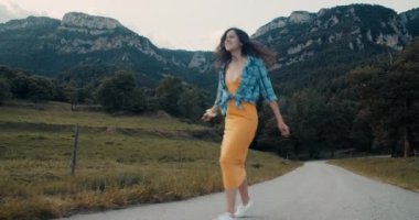 Mutlu çekici genç kadın yaz yolculuğunda boş dağ yolunda yürüyor ve etrafında dönüyor. Yolculukta neşeli, ilham verici bir kız ol. Aktif yaşam tarzı ve seyahat tutkusu