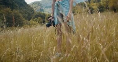 Tanımlanamayan kadın fotoğrafçı çayırda duruyor ve elinde fotoğraf makinesi var. Tek başına gezen kadın, dağdaki yaz yolculuğunda fotoğraf ekipmanıyla..