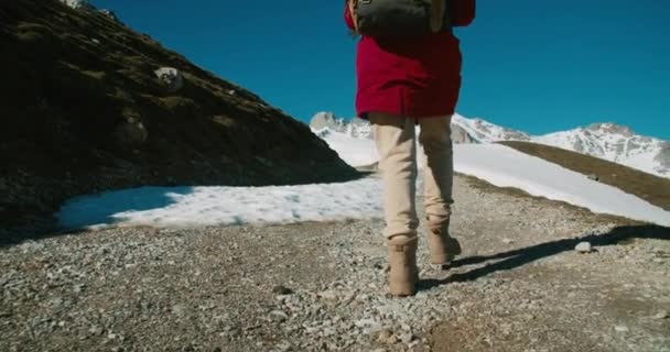 手持ちのローアングルカメラの旅に女性ハイカーに従ってください バックパックとブーツ登山山と赤いジャケットの女性 旅行者は休暇でアクティブなライフスタイルをリードしています 旅行での閉鎖の足跡 — ストック動画