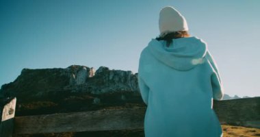 Genç yetişkin kadın bahar yolculuğunda destansı dağ manzarasına bakan tepenin üstünde duruyor. Aktif yaşam tarzı ve seyahat tutkusu. Yolculukta gün batımında çitlere yaslanan kadın gezgin