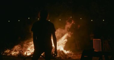 Genç yetişkin adam silueti Saint John partisinde büyük şenlik ateşini izliyor. Geceleri dışarıdaki yangını kontrol ederdi.