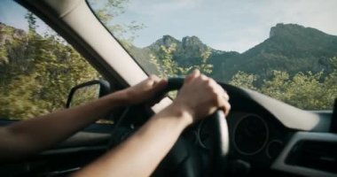 Woman hands closeup holding steering wheel on journey adventure. Young adult female driving vehicle on mountain road on summertime road trip. 