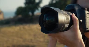DSLR kamerasını tutan kadın elleri odak uzaklığını değiştiriyor ve odaklanıyor. Fotoğrafçı kadın yakın çekimde seyahat ederken fotoğraf çekiyor. Gezgin blogcu, blog veya sosyal medya için dijital içerik çekiyor