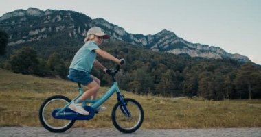Yaz tatillerinde bisikletle boş dağ yolunda bisiklet süren bir çocuk. Kaygısız mutlu çocuklar kır yolunda bisiklet sürüyor. Tatilde çocukluk. Çocuk akşam çayırda bisiklet sürüyor.. 