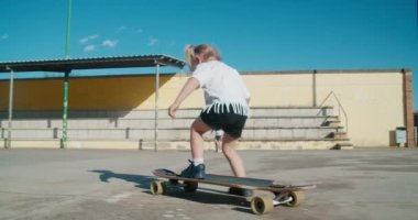 Joyful carefree toddler girl learning to ride on skate longboard on sport field on summertime. Happy and brave child enjoy extreme sport. Concept of active and healthy childhood