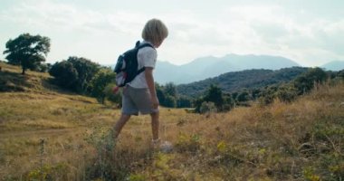 Hike journey to mountain of little child on summer vacations with backpack. Young explorer walk at evening surrounded by beautiful nature. Children on summertime trip. 