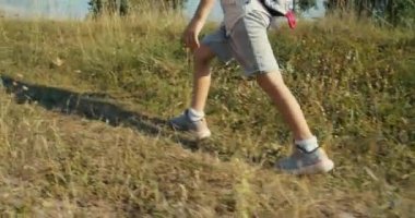 Düşük açılı kamera, yaz tatillerinde yürüyüşe çıkan çocuğu takip ediyor. Kapalı çocuklar akşamları çimlerin üzerinde yürür. Şort ve spor ayakkabıların üzerindeki çocuk ayak sesleri. 