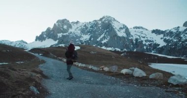 Erkek gezgin dağ yolunda sırt çantasıyla yürüyor ve tatil sırasında kızını boynuna takıyor. Küçük kız yürüyüş gezisinde babanın boynuna oturur. Aile destansı dağ manzarasında yürür