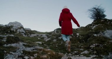 Kırmızı ceketli kadın dağa tırmanıyor ve ellerini başarıyla kaldırıyor. Gezgin kadın, tatil gezisindeki özgürlüğü hissediyor. Kamera kayalıklarda koşan kızı takip ediyor.