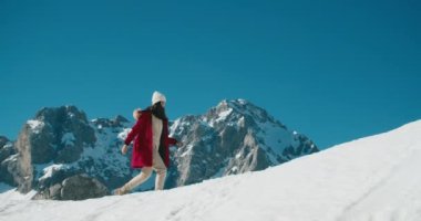 Traveler female in red puff jacket walk on snowed mountain top. Young adult woman on vacation travel hiking and climbing hill. 