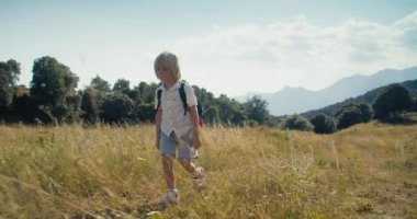 Children walk on mountain meadow at vacation travel. Child boy with backpack hiking on summer journey. Healthy and active lifestyle and carefree childhood. 