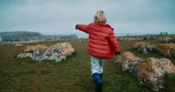 Children Orange Puff Jacket Walk Cliff Meadow Pointing Hand Ocean — Stockvideo