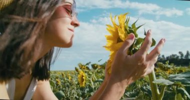 Romantic joyful girl smelling sunflower on field at sunny day and smile. Tourist female portrait on summer vacation at flowers meadow. Young lady feeling happy on summertime travel