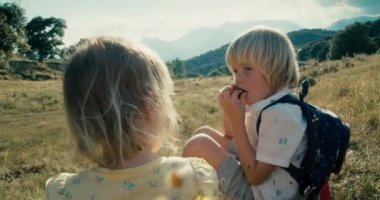 Two children sitting on hill eating cherry fruit on beautiful mountain landscape. Cute sister and brother on vacation summertime trip. Family together on journey adventure