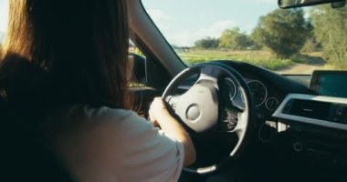 Handheld slow motion medium shot of traveler female driving car on road trip to mountain forest. Young adult brunette woman back view drive vehicle on country road. 