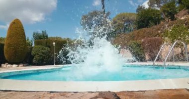 Carefree playful guy jump into the swimming pool on summertime travel. Man on summer vacation having fun in the pool. Static slow motion footage water splashes and joyful people