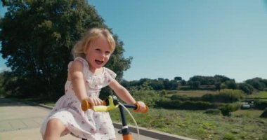 Toddler girl in dress drive bike on sunny summer day. Happy children riding balance bicycle along the agricultural meadow on rural environment. Carefree childhood on countryside. 