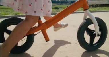 Happy child riding balance bicycle along the agricultural meadow on rural environment. Toddler girl in dress drive bike on sunny summer day. Carefree childhood on countryside. 