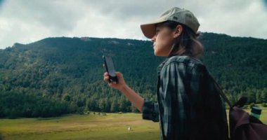 Portrait of female traveler on tourist path taking photography on smartphone during her vacation hike travel adventure. Young adult woman blogger or influencer make digital content on her mobile phone
