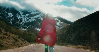 Kış tatili macerasında ilham veren mutlu kadın destansı manzarası olan boş dağ yolunda yürüyor. Neşeli gezgin kadın ellerini kaldır ve hafta sonu gezisinde etrafında dön.