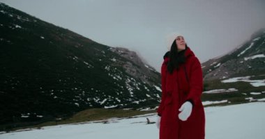 Kış tatili macerasında kar üzerinde yürüyen kırmızı ceketli kadın gezgin yavaş çekimde çekilmiştir. Turist gezisinde mutlu genç kadın yürüyüşü. Bulutlu bir günde hafta sonu seyahatinde neşeli bir kız. 