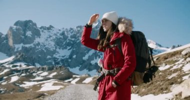 Kırmızı ceketli sırt çantalı kadın kış yolculuğunda turist dağları yolunda yürüyor. Güneşli soğuk bir günde sırt çantasıyla gezintiye çıkmış bir kadın. Aktif ve sağlıklı yaşam tarzı