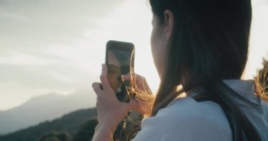 Dağ yolculuğunda akıllı telefon kullanan bir bayan yolcu. Güneş ışığı altında cep telefonuyla fotoğraf çeken bir kadın. Dijital içerik oluşturan gezgin blogcu ya da etkileyiciName
