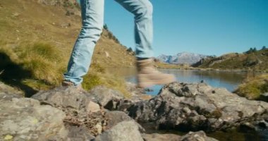 Turist ayağı, hafta sonu macerasında dağ nehrinden göle akan yürüyüş ayakkabılarıyla yakınlaşır. Sırt çantalı gezgin kadın aktif ve sağlıklı bir hayat sürüyor.