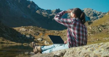 Gezgin kadın, dizüstü bilgisayar kullanarak göl kıyısında güzel bir dağ manzarasıyla oturuyor. Tatil gezisinde serbest çalışan bir işçi, klavyede daktilo kullanıyor. Görev dışı özgürlük 