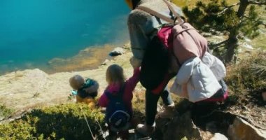 Çocuklu bir kadın tatilde macera peşinde tepeden aşağıya, güzel dağ gölüne tırmanıyor. Aile seyahati güneşli bir günde göl kıyısına doğru yürür.. 