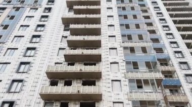 Üst kattaki evin inşaatı, koruyucu kasklı işçi ön cephe, inşaat vinçleri, alttaki pencereli beton bloklar, bulutlu hava, büyük bir gayrimenkul.