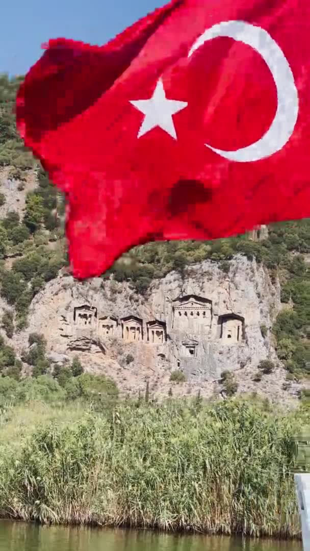 Вертикальні кадри мальовничого пейзажу національного парку Далянь в Туреччині, гробниці королів Кауноса, пасажирські човни, гори на задньому плані, розмахуючи прапором індички. — стокове відео