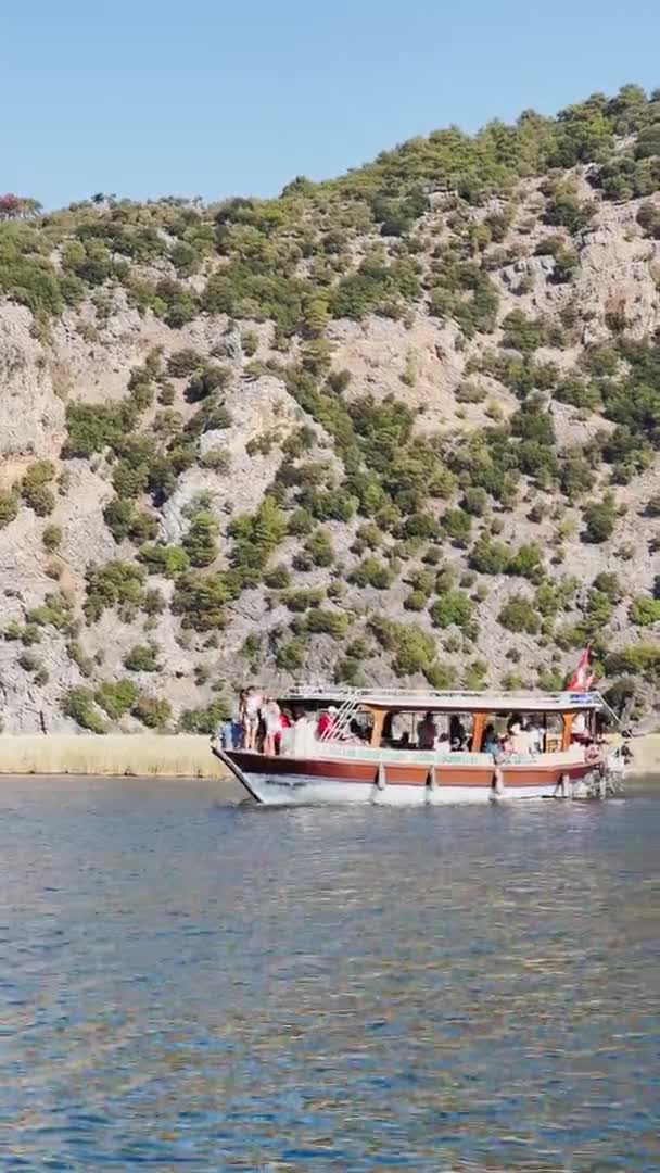 Турция, Далянь, 06 октября 2021 года: Живописный залив Далянь в Турции, Каунос Могилы царей ориентир, пассажирские лодки, горы на заднем плане, размахивая флагом индейки — стоковое видео