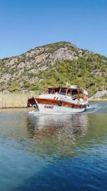 Türkiye, Dalyan, 06 Ekim 2021: Türkiye 'de Dalyan' ın pitoresk körfezi, Kralların Tarihi Kaunos Mezarları, yolcu botları, arka planda dağlar, el sallayan hindi bayrağı