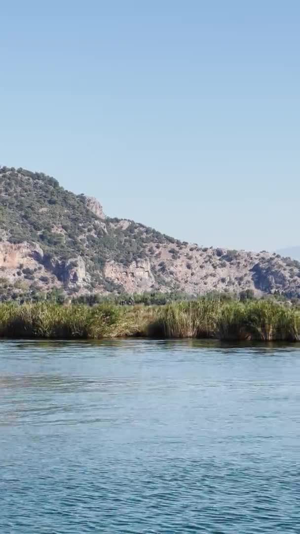 Κατακόρυφα πλάνα από το γραφικό τοπίο του Εθνικού Δρυμού του Dalyan στην Τουρκία, Τάφοι Caunos των Βασιλέων ορόσημο, επιβατηγά πλοία, βουνά στο παρασκήνιο, κυματίζει σημαία γαλοπούλας — Αρχείο Βίντεο